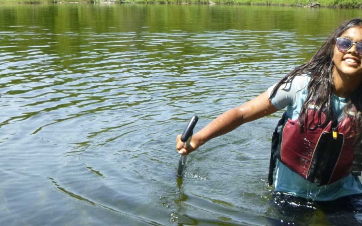 A person wearing a life jackets stands in waist-deep water and smiles